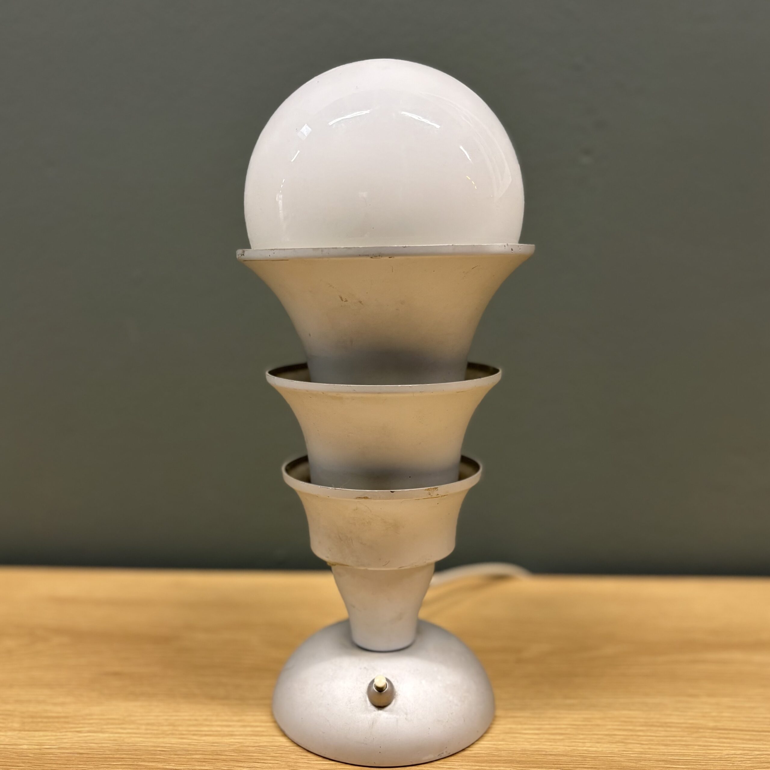 Lampada da tavolo vintage con base circolare, fusto a tre elementi conici sovrapposti e sfera luminosa opaca, su tavolo in legno.