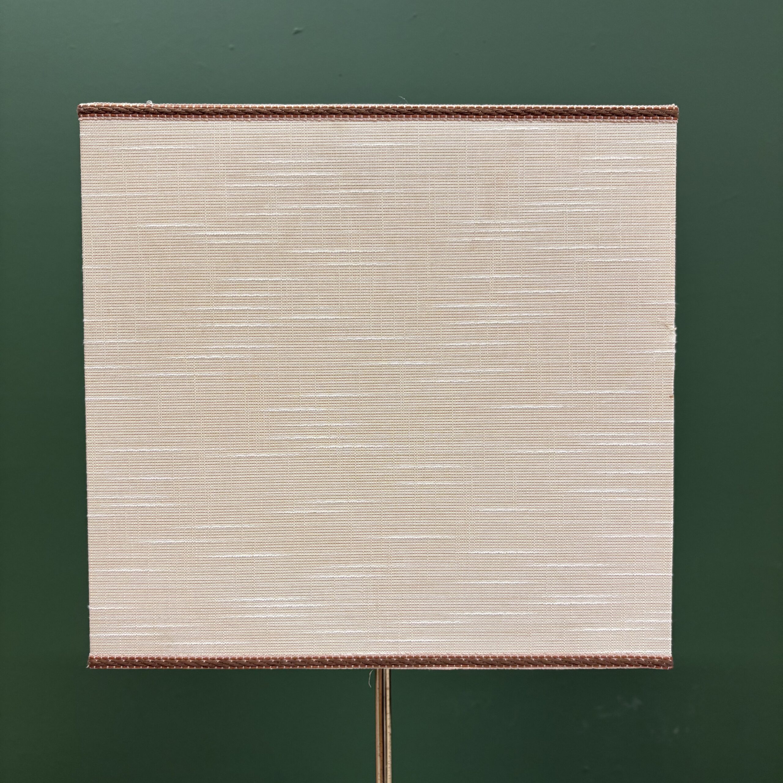 Paralume quadrato in tessuto beige chiaro con trama orizzontale e bordo intrecciato marrone scuro, su sfondo verde scuro.