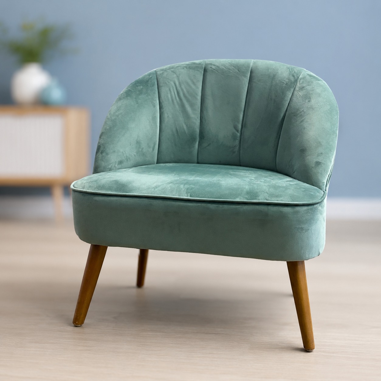 Poltroncina accentata in velluto verde acqua con schienale a coste e gambe affusolate in legno, su pavimento chiaro.