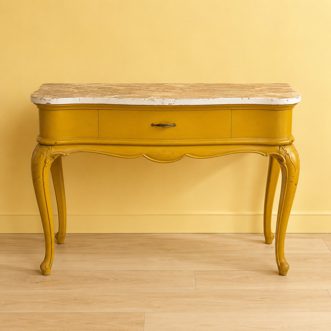 Consolle vintage gialla con finitura invecchiata, piano effetto marmo, un cassetto e gambe cabriole intagliate, su sfondo giallo.