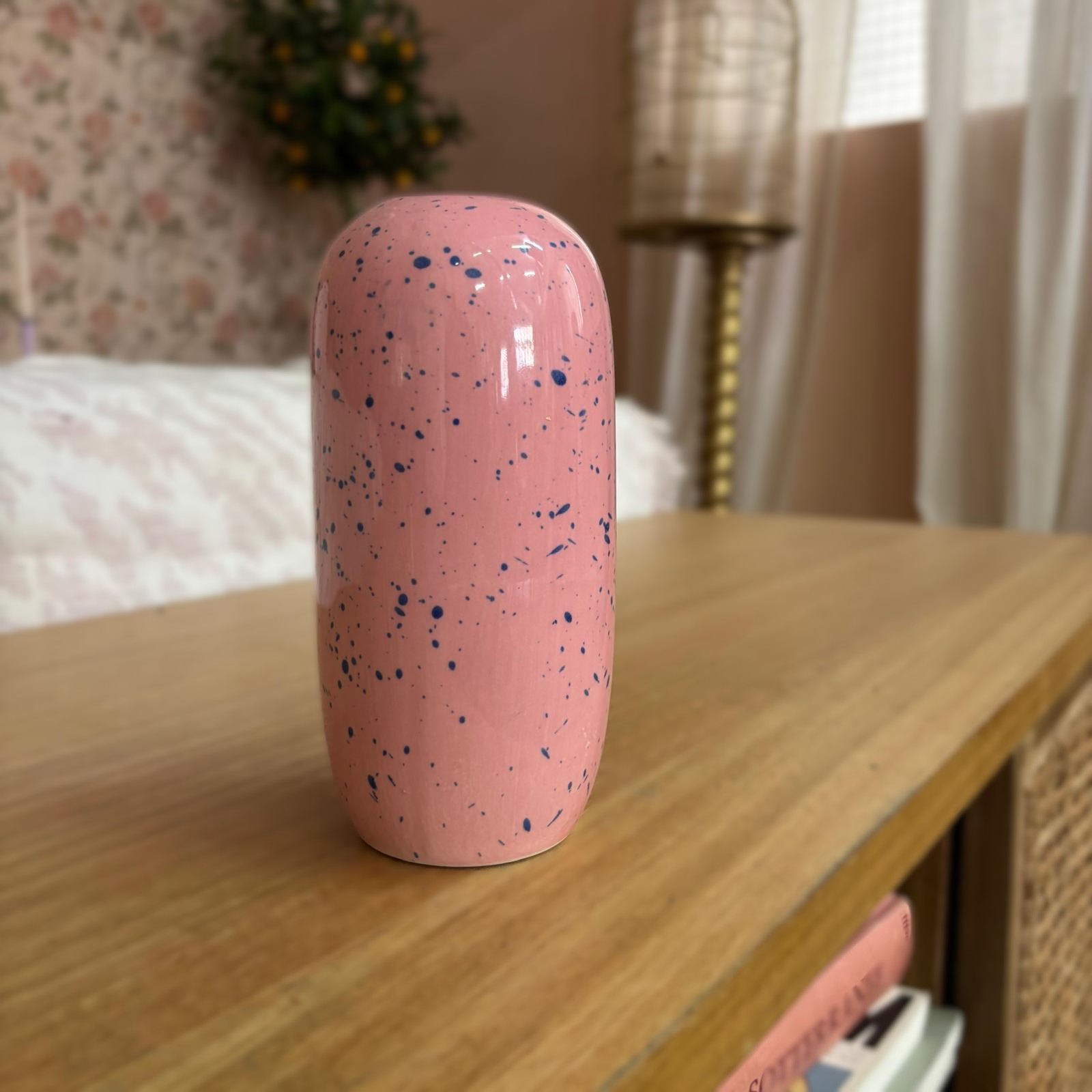 Vaso cilindrico in ceramica rosa con finitura speckled blu, posizionato su un comodino in legno chiaro.