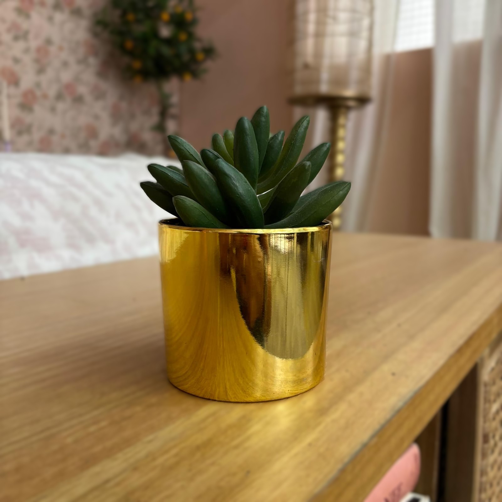 Pianta grassa artificiale con foglie verdi in un vaso cilindrico color oro lucido, posizionata su una superficie di legno chiara.
