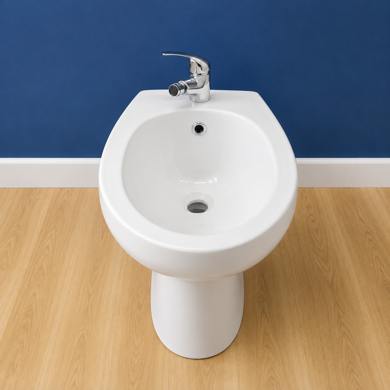 Bidet in ceramica bianca lucida con rubinetteria cromata, posizionato su pavimento in legno chiaro davanti a una parete blu.