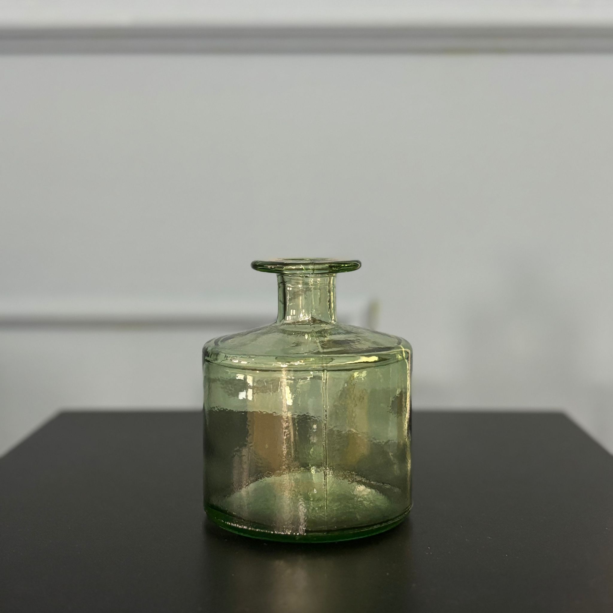 Vaso decorativo in vetro di colore verde tenue, con corpo cilindrico e collo stretto, posizionato su una superficie scura.