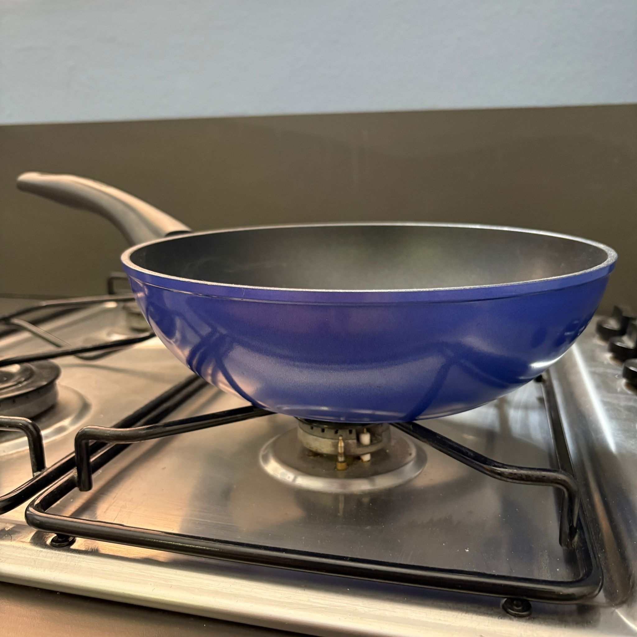 Padella antiaderente blu con manico grigio scuro posizionata su un fornello a gas in acciaio inossidabile.