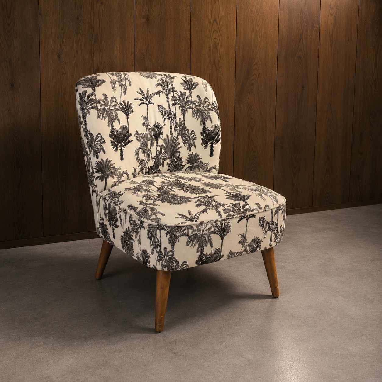 Poltroncina slipper imbottita con tessuto a stampa tropicale bianco e nero (palme e tigri), gambe in legno chiaro, su pavimento grigio e parete in legno scuro.