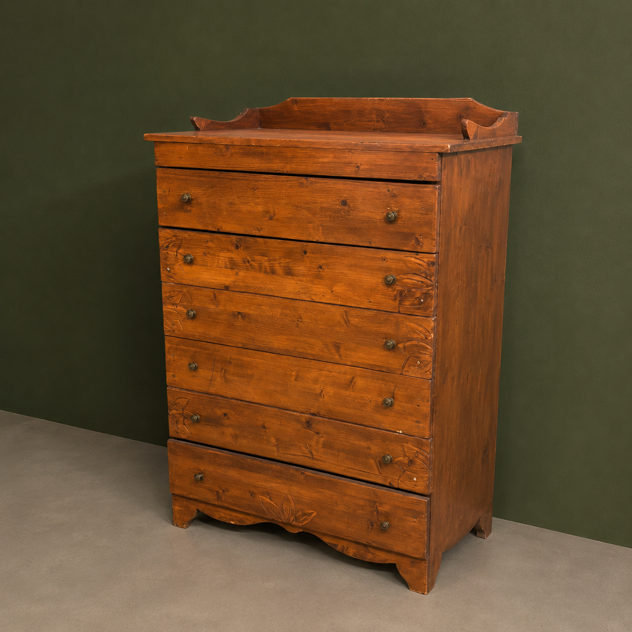 Cassettiera alta in legno massello di colore marrone rossiccio con sei cassetti, maniglie a pomello e intagli decorativi sulla base.